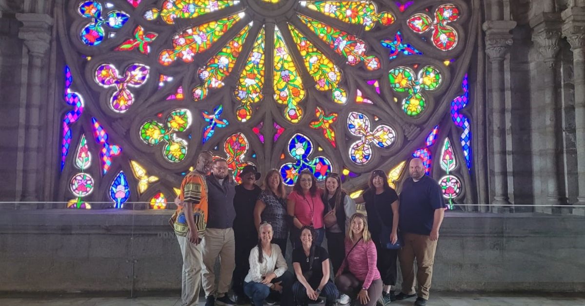 A group of people standing in front of a colourful stained-glass window in a basilica.