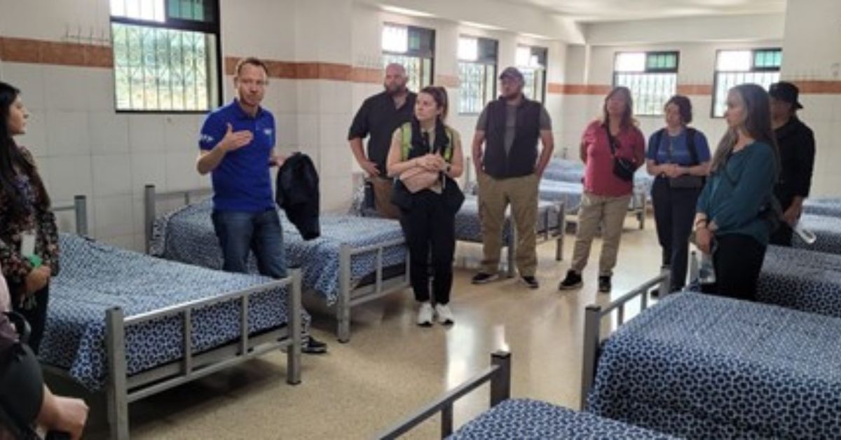 Students standing among a row of neatly made beds.