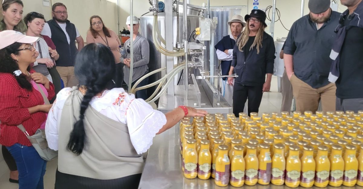 A group of students gathered around a table in a factory looking at bottles of non-fermented corn drink.