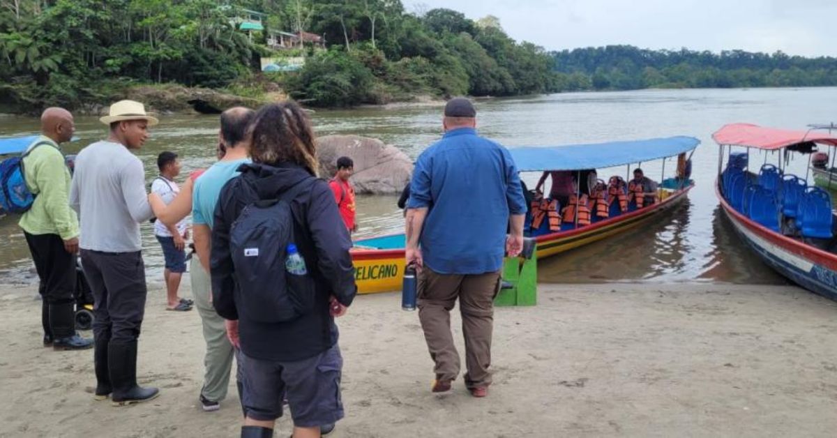 A group of students standing on the shore in front of two canoes.