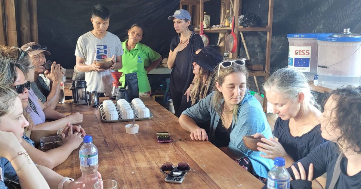 People sitting around a wooden table sampling coffee.