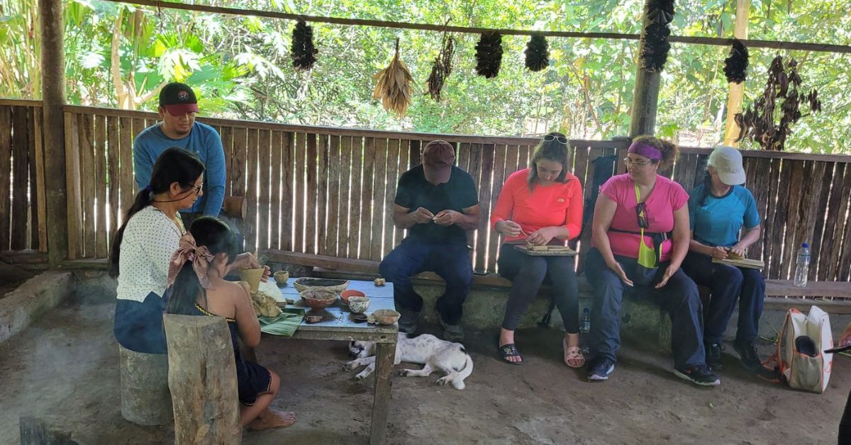 A group of students sitting on a bench working on pottery in their hands.