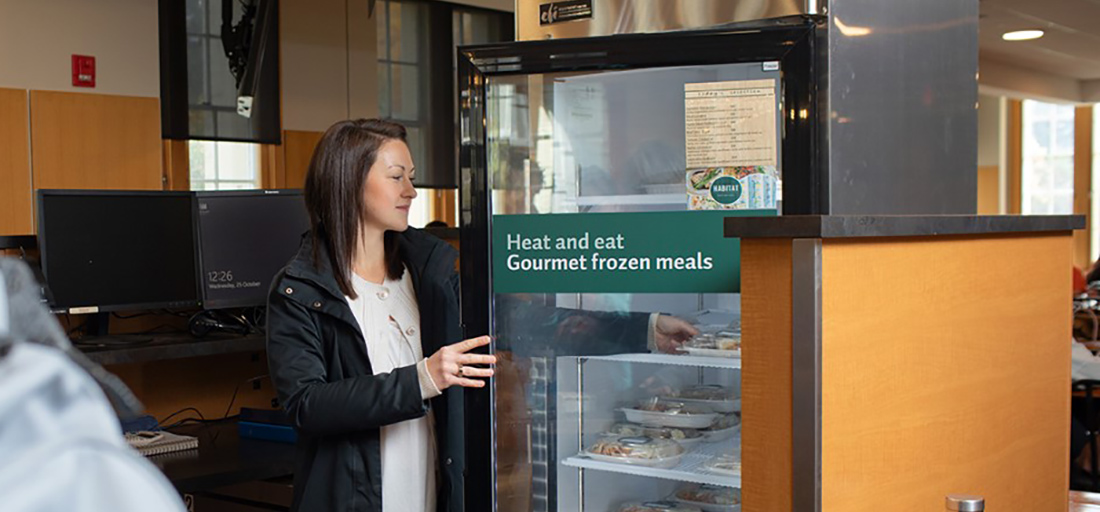 A person reaches into a fridge full of grab-and-go food options at Habitat Cafe