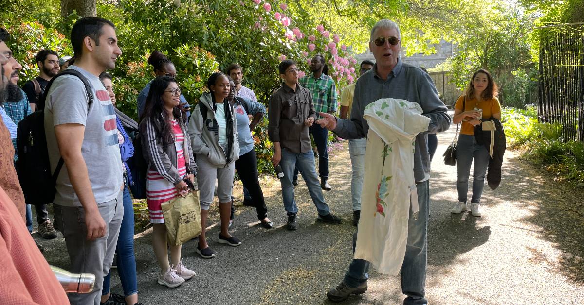 Students standing in garden, looking at teacher.