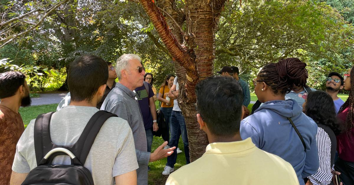 Students looking at tree trunk, listening to teacher.