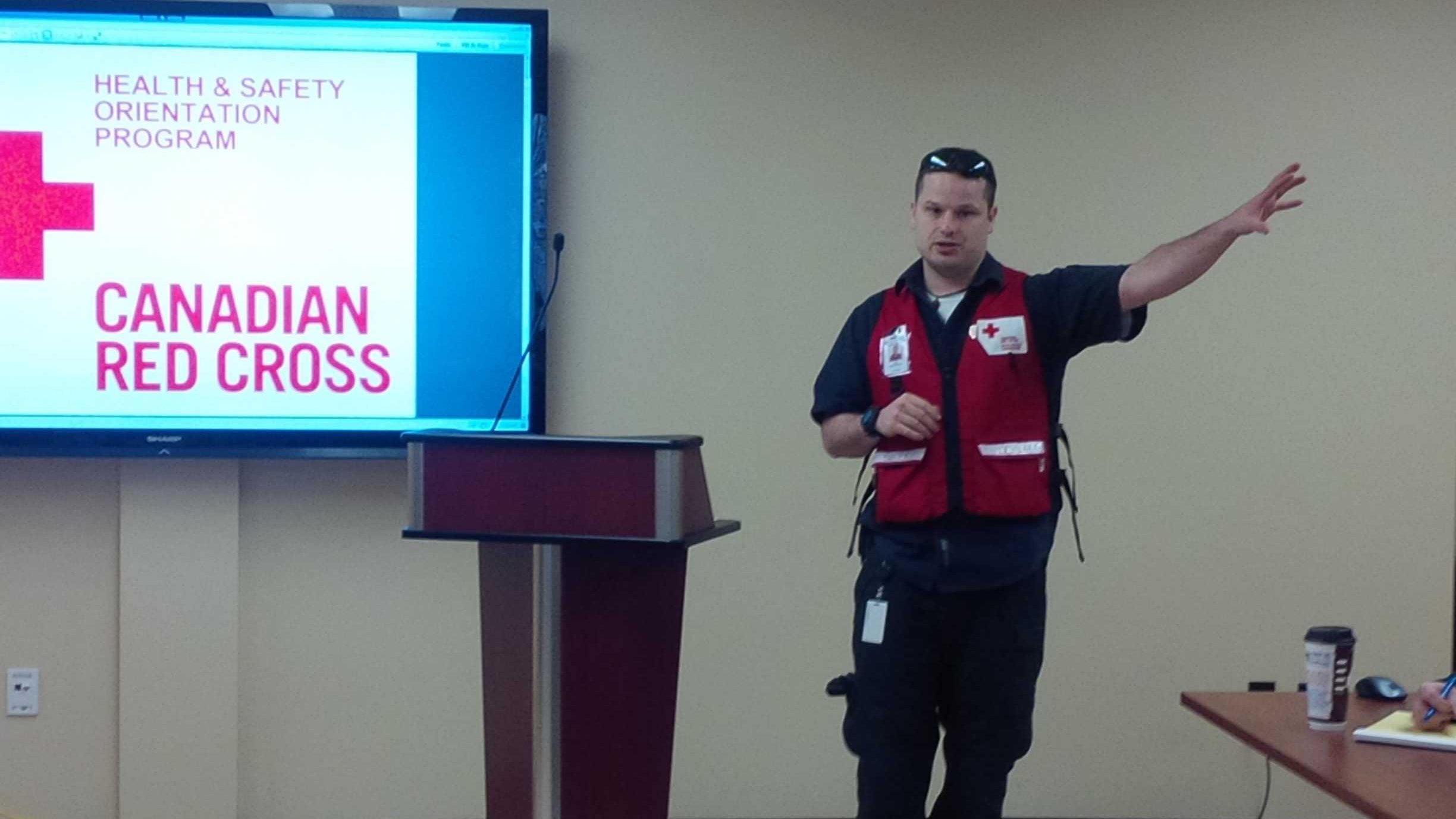 Man giving a presentation, wearing a red, Red Cross vest.