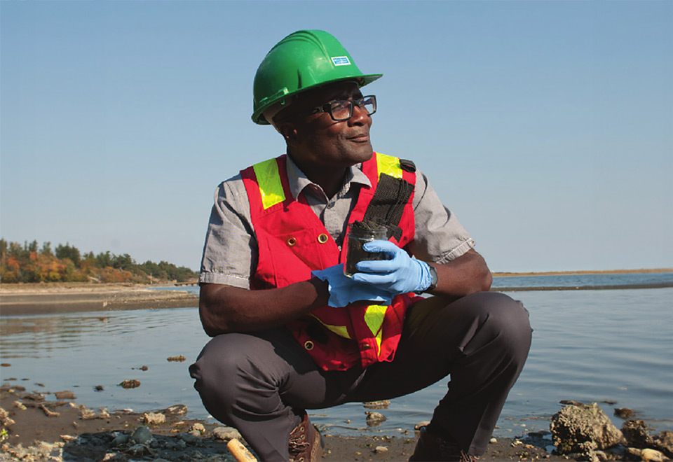 RRU researcher squats on the pacific shoreline wearing PPE, looking out at the horizon