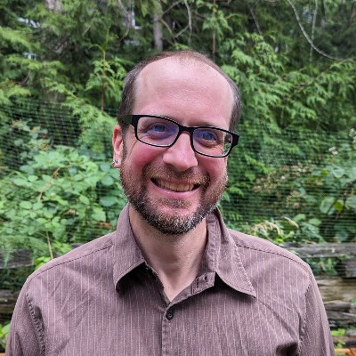 Rob Newell smiling at the camera. He is wearing glasses and a brown shirt. 