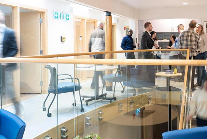 A link to more information about ways to give to talent and research at RRU. The image shows a bustling, modern office space with faculty members and students buzzing around and with a discussion in the background