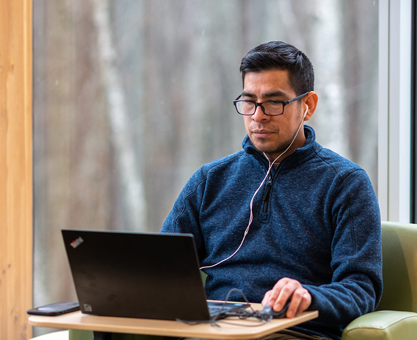 RRU student sites by a large window on his laptop and works intently.