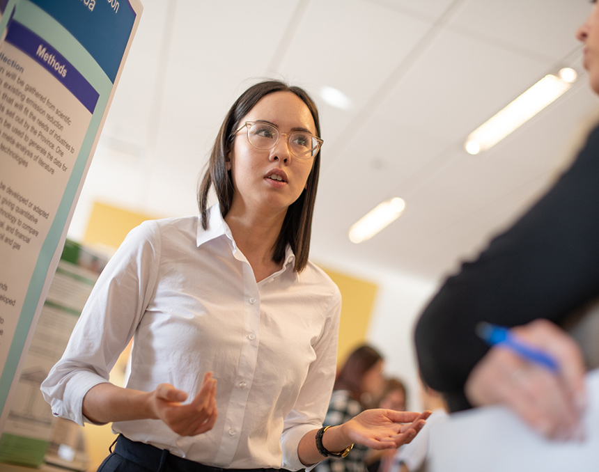 An RRU student stands in front of her academic poster and engages in conversation
