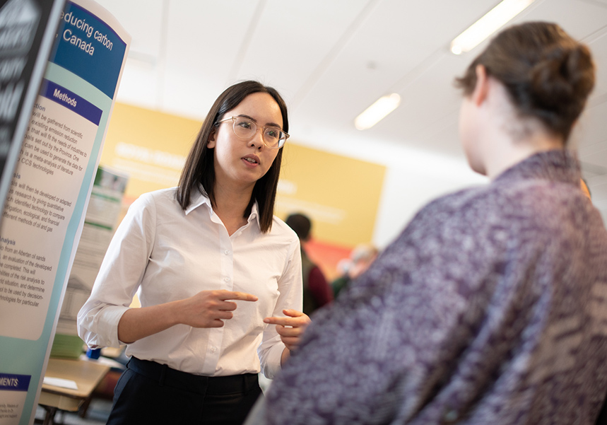 RRU student researcher discusses their research poster with an observer passing by