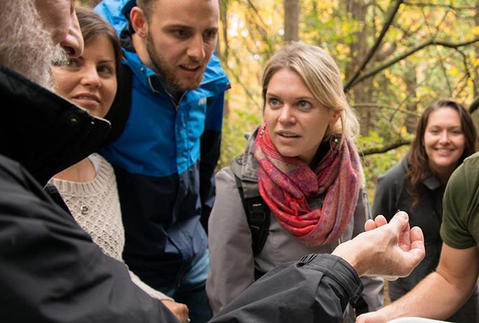 A link to more information about ways to give to talent and research at RRU. The image shows a group of master's students gather in a wooded areas and listen to their instructor speak