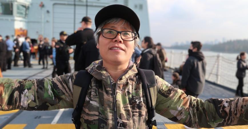 Jessie Zhang wearing dark rimmed glasses and ballcap and standing on the deck of a navy vessel.