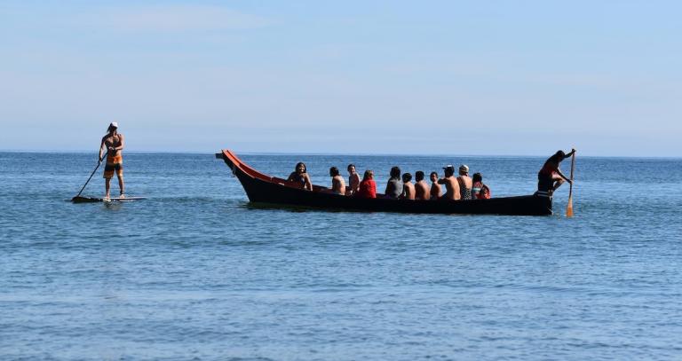 Swimming instructor and First Nation community members learn drowning prevention in a traditional canoe on the water.