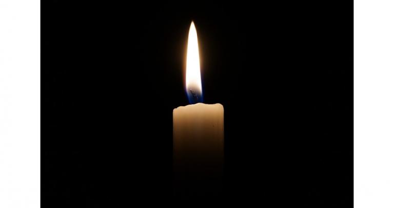 A lit white candle glows against a dark background
