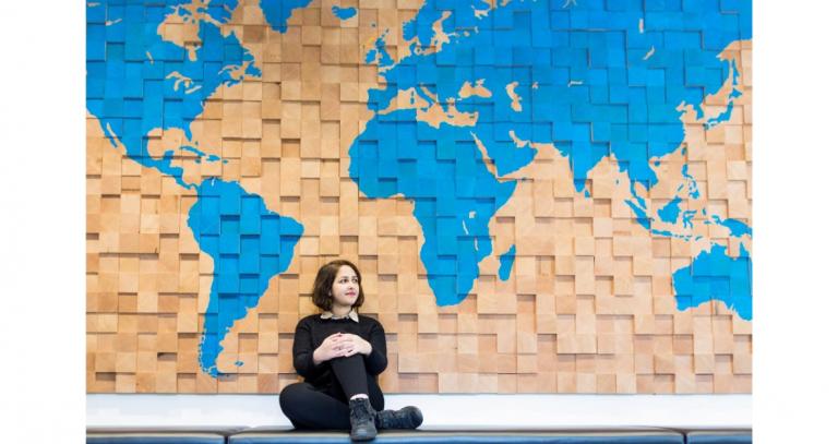 Student-Negar-Abedi-sitting-in-front-of-wood-world-map-wall