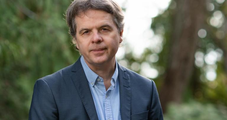 David Black, standing in front of trees in a dark grey suit jacket and blue button up shirt 