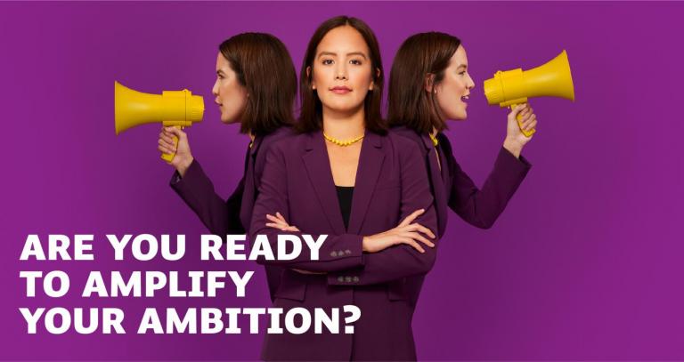 A person in a purple suit, with two of the same person behind them holding yellow microphones. The background is a bold purple. The text reads: "Are you ready to amplify your ambition?"