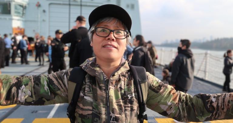Jessie Zhang wearing dark rimmed glasses and ballcap and standing on the deck of a navy vessel.