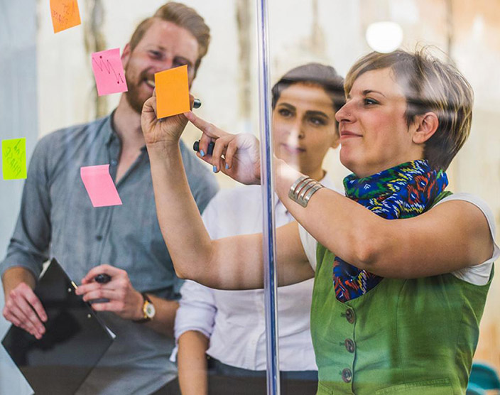 An RRU student stands with their peers in front of a glass wall, placing sticky notes together.