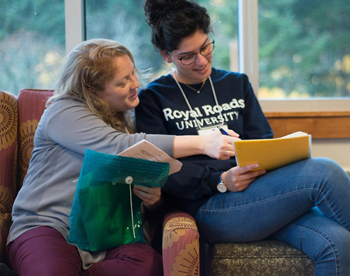 Two RRU students sit next to each other in lounge chairs looking at their study notes.