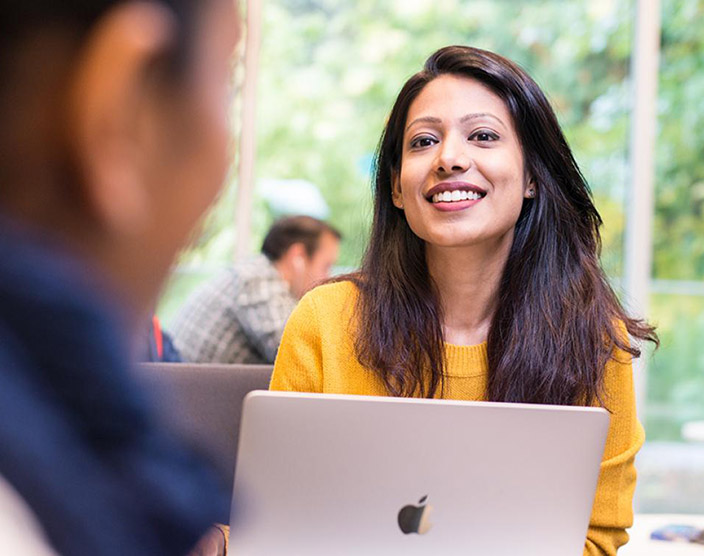 An RRU student smiles and looks on while sitting on their laptop.