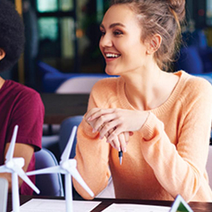 A group of BBA students huddle over a large table to assemble a tower made of pasta.
