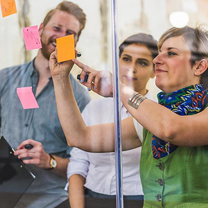 An RRU student stands with their peers in front of a glass wall, placing sticky notes together.