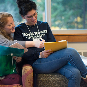 Two RRU students sit next to each other in lounge chairs looking at their study notes.
