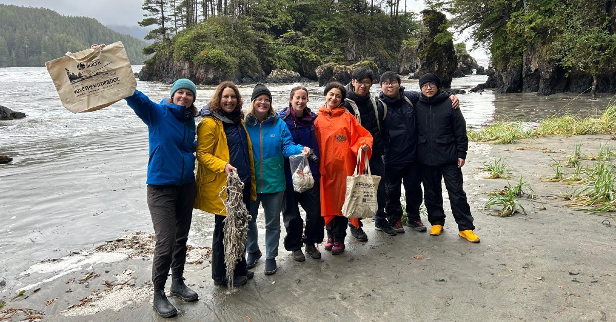 Group of students and faculty stand on the beach holding up items they found during a shore clean-up.