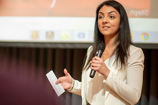 A BA in Professional Communication student presents in front of an audience holding a microphone.