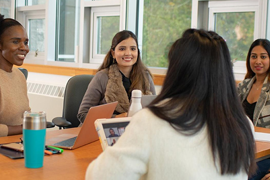 A table of students in an RRU classroom looks at each other in conversation while sitting with their laptops