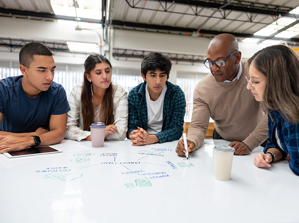 An instructor walks their students through a table-top white board in a large classroom