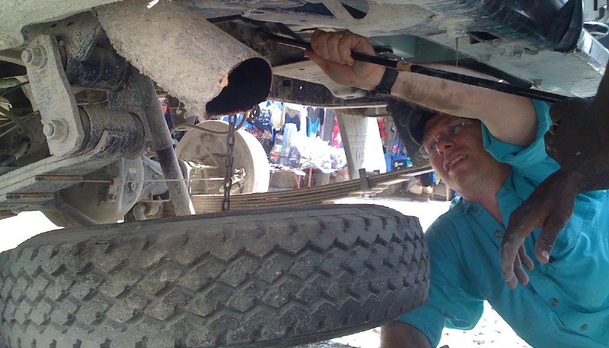 Man crouched under car, holding a wrench and working on the chassis.
