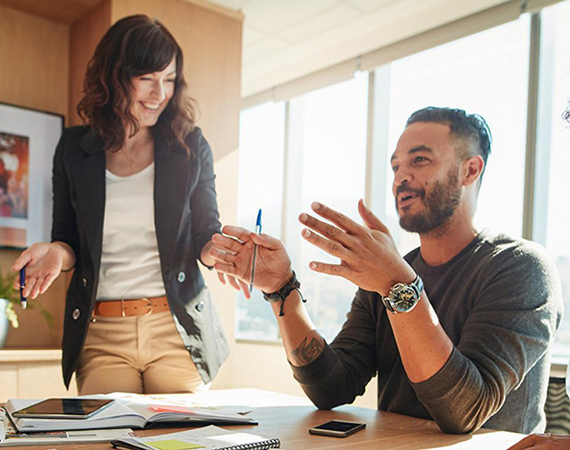Three students exchange words around a table, in an animated conversation. This image links to the Graduate Certificate in Change Management.
