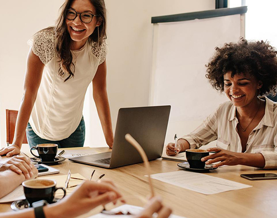 A group of students sit around a wooden table with their laptops. This image links to the Graduate Certificate in Corporate Social Innovation