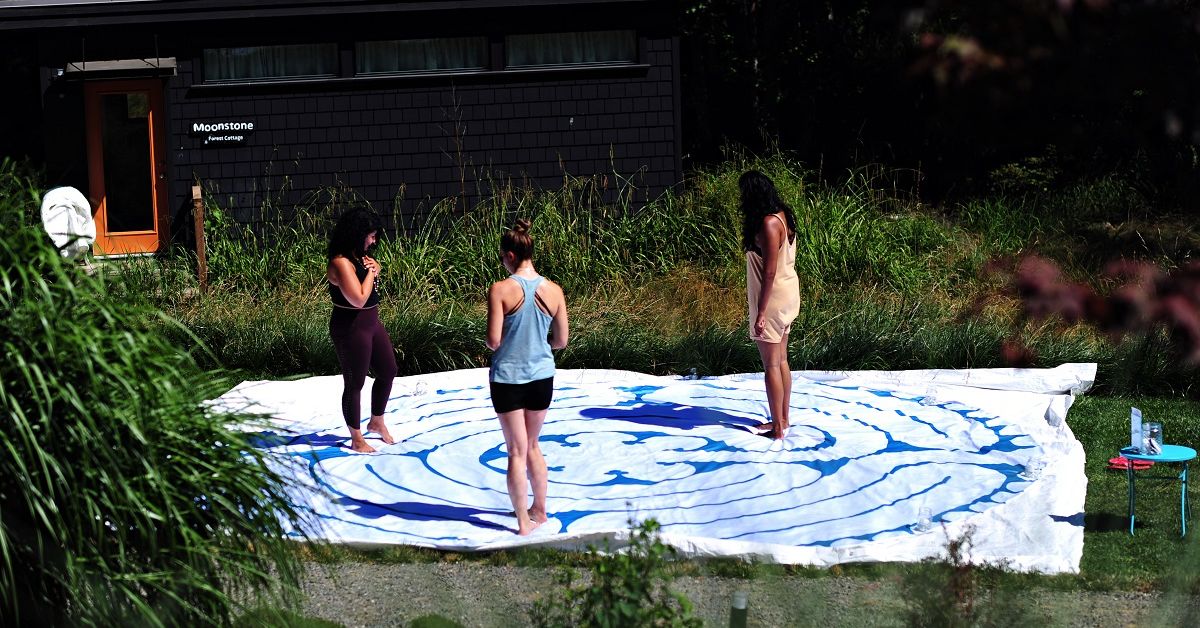 three women standing at different points on a canvas labyrinth