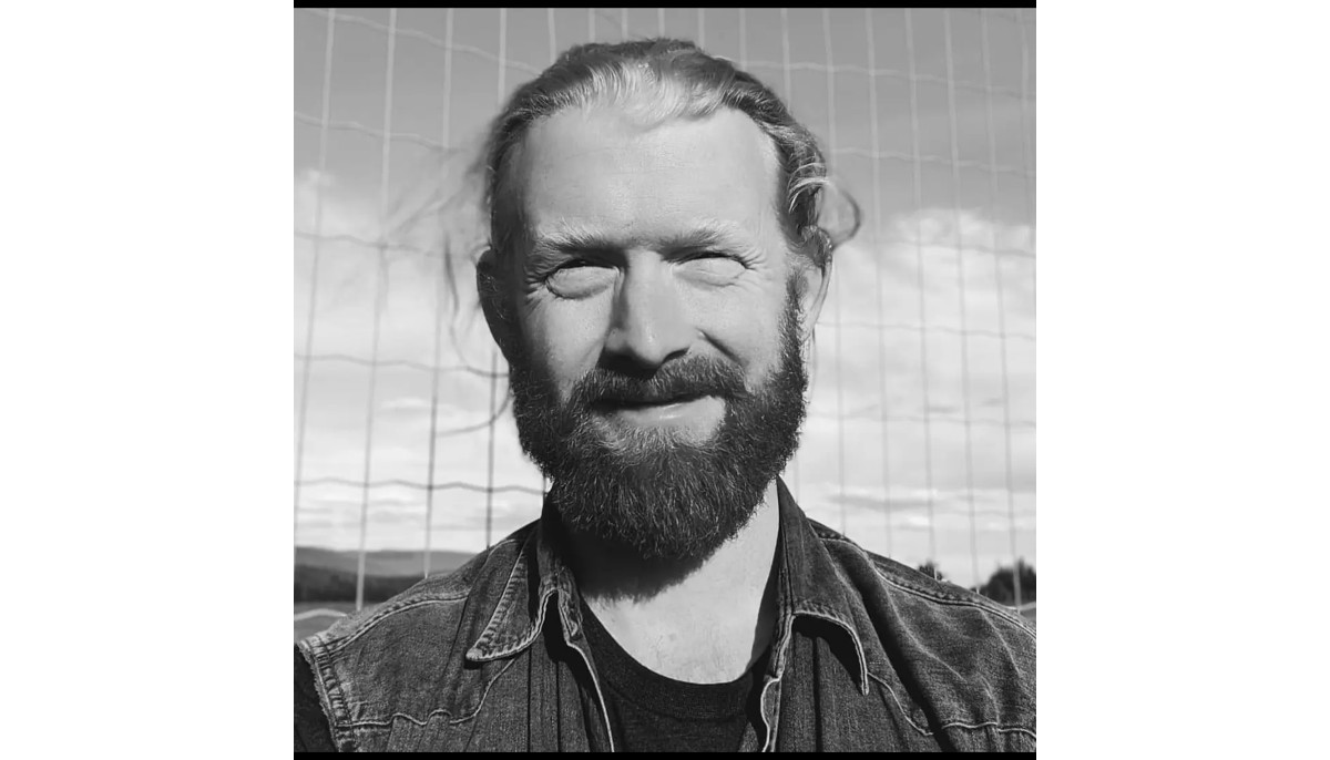 Black and white close up image of a bearded man smiling at camera.