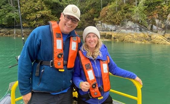 A student and field school instructor pose for a photo wearing life jackets while on a boat.