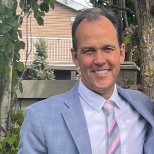 Stephen Camp wearing a grey suit with a pink and grey striped tie.