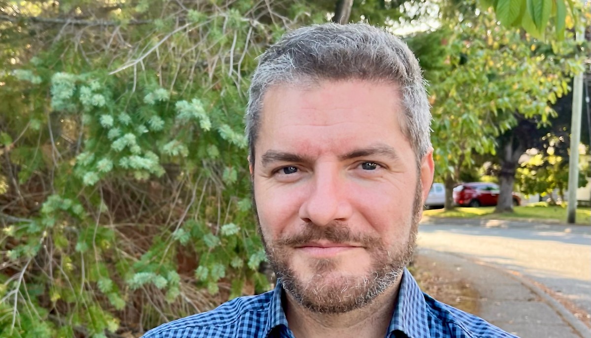 Man standing in front of tree, looking into the camera.