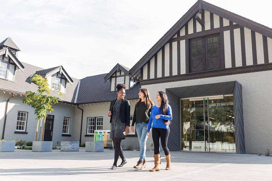 Three students walk in front of a building on campus at Royal Roads University