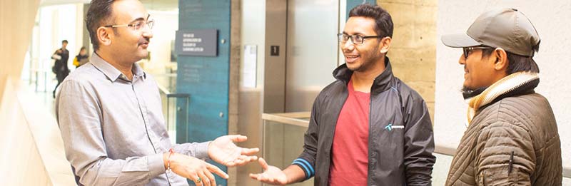 Three students stand in discussion in the hallways at Royal Roads University.