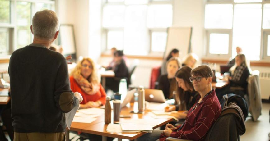 A faculty member stands at the head of a classroom full of students. 