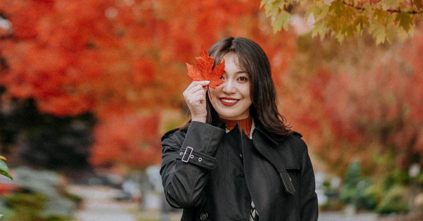 Alum Wendy Wang in the fall foliage holding a maple leaf in front of her eyes.