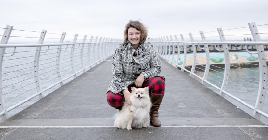 Portia Zaffaroni kneels with her dog on a walking bridge over water