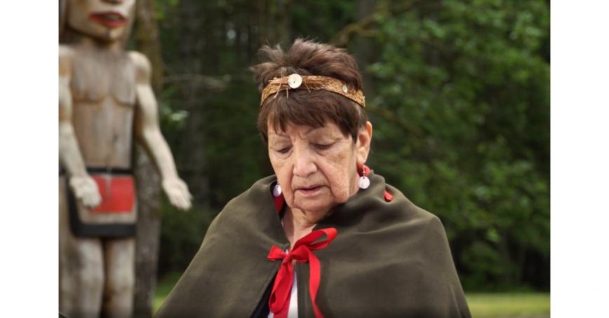 Elder Shirley Alphonse delivers opening prayer outdoors with totem pole in background