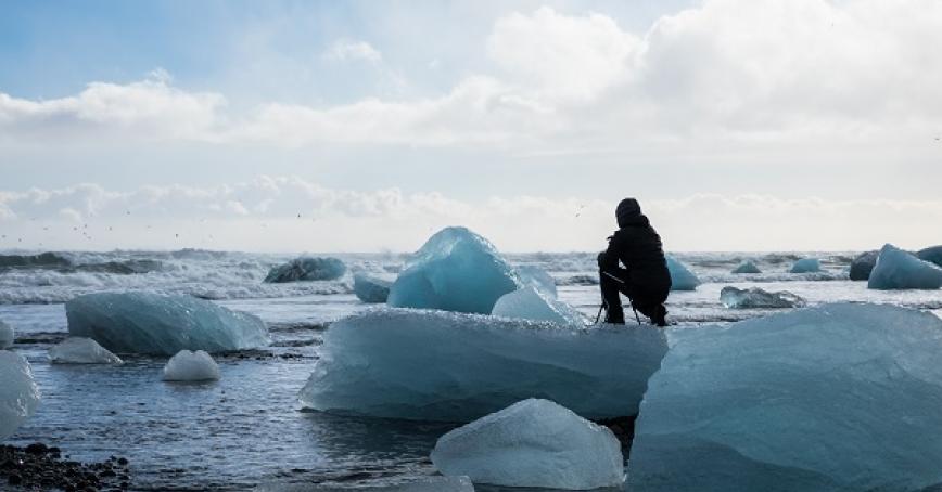A person crouches down on an ice float. 