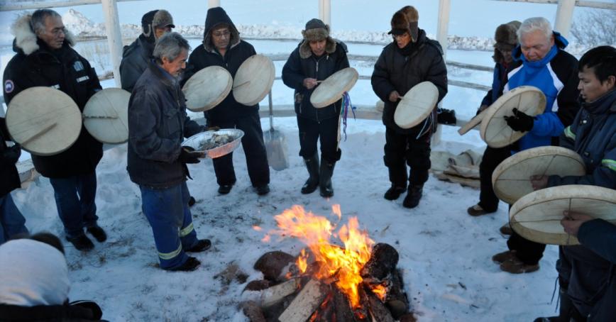 A group of people drumming around a fire on a snowy day